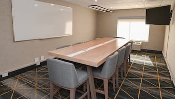 A conference room with a long table, six chairs, a whiteboard, a projector screen, and a patterned carpet.