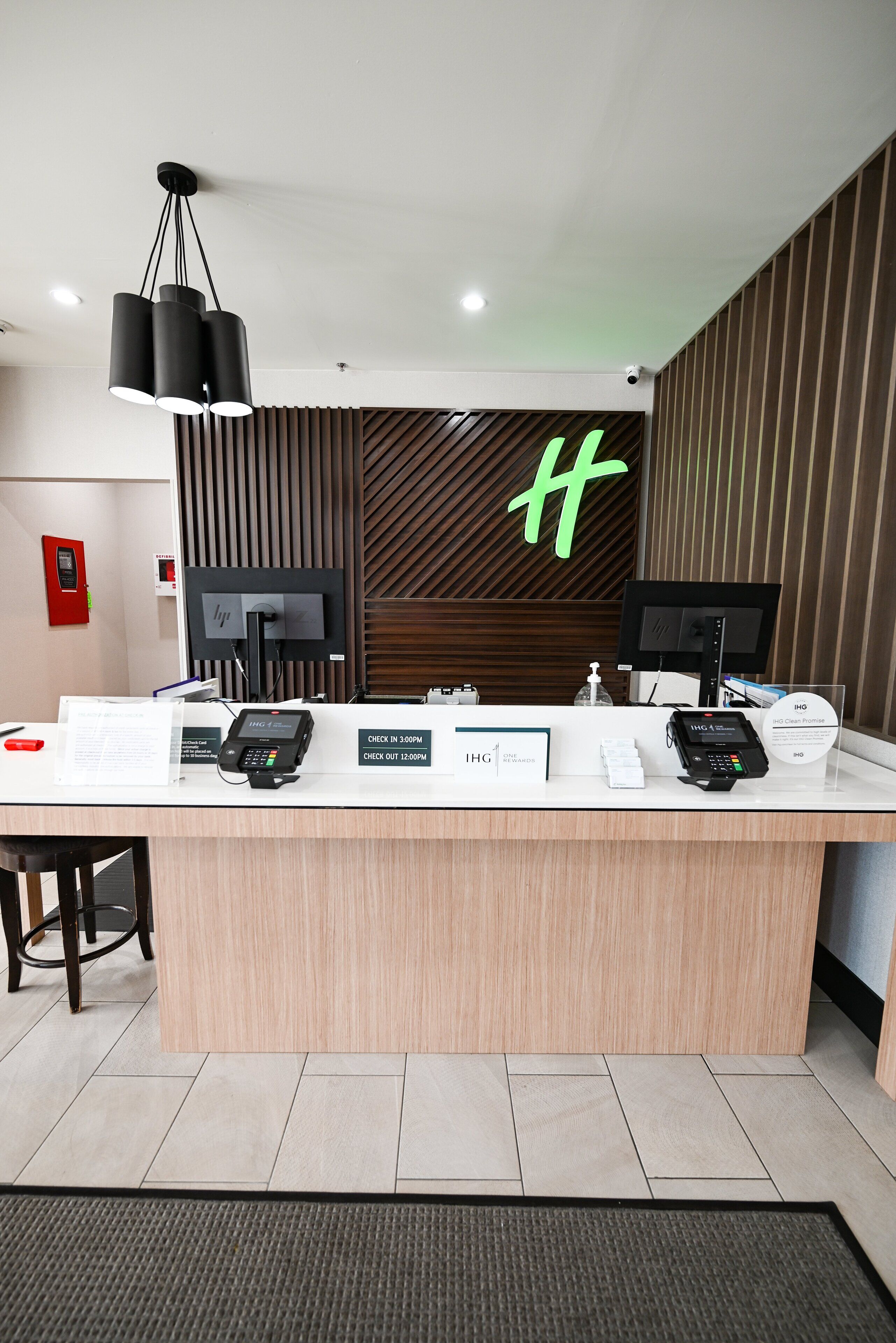 Ein Hotelrezeptionsschalter mit modernem Design, darunter eine Wandpaneele aus Holz, ein großes grünes Logo und mehrere Zahlterminals.