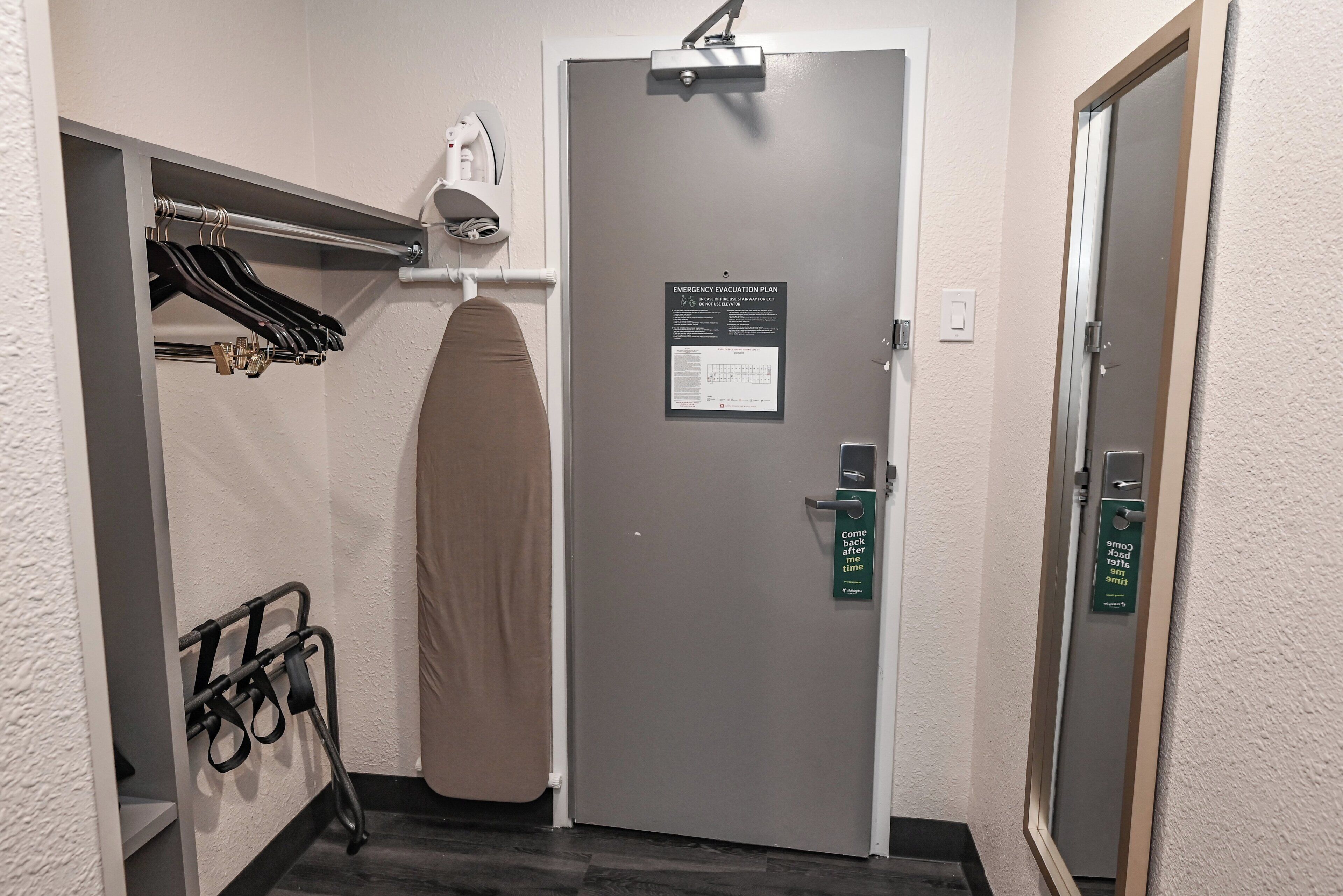 A hotel room with a grey door, a towel rack with hanging towels, and a sign indicating an emergency evacuation plan.