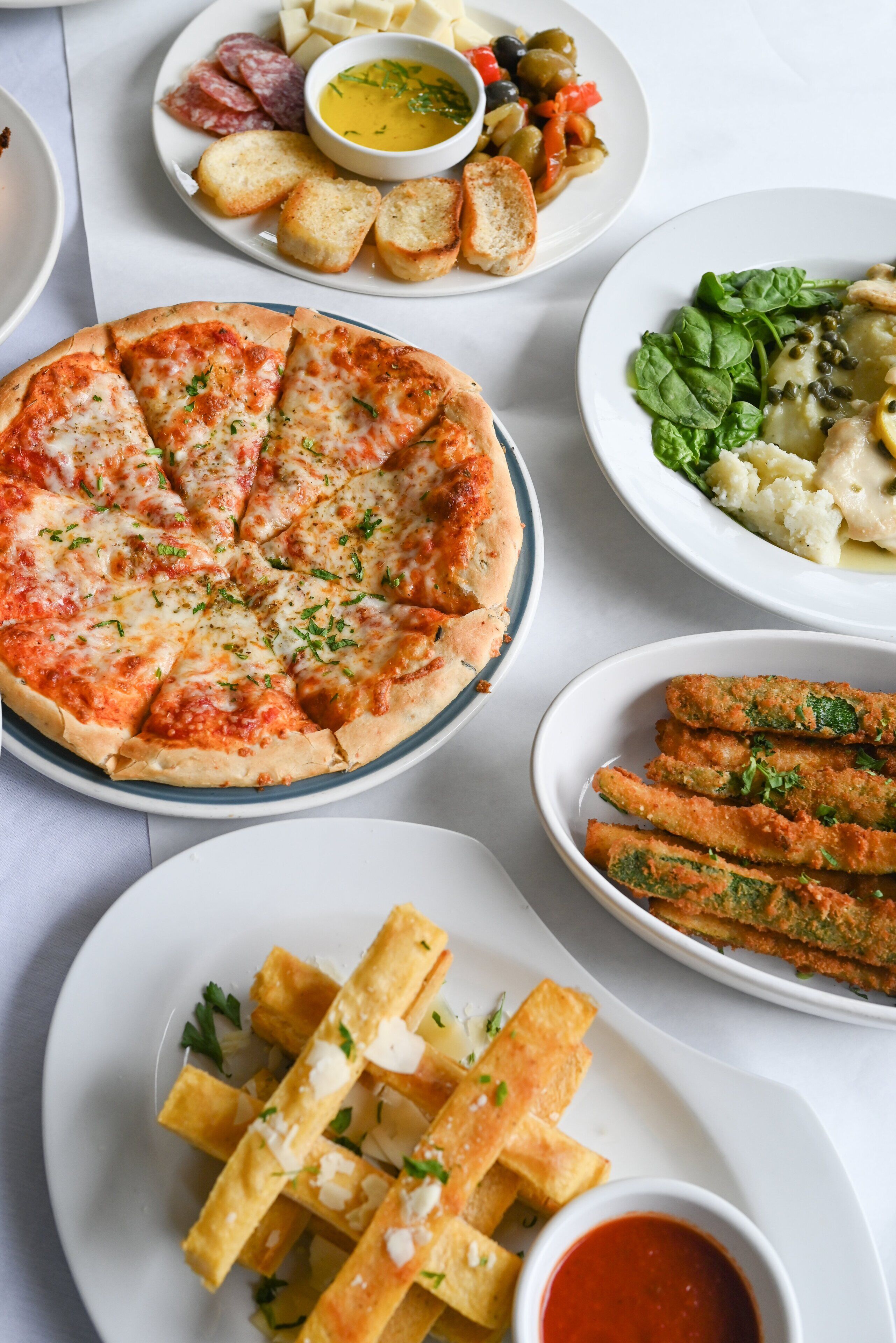 A variety of dishes including a pizza, bread, and a salad on a table.