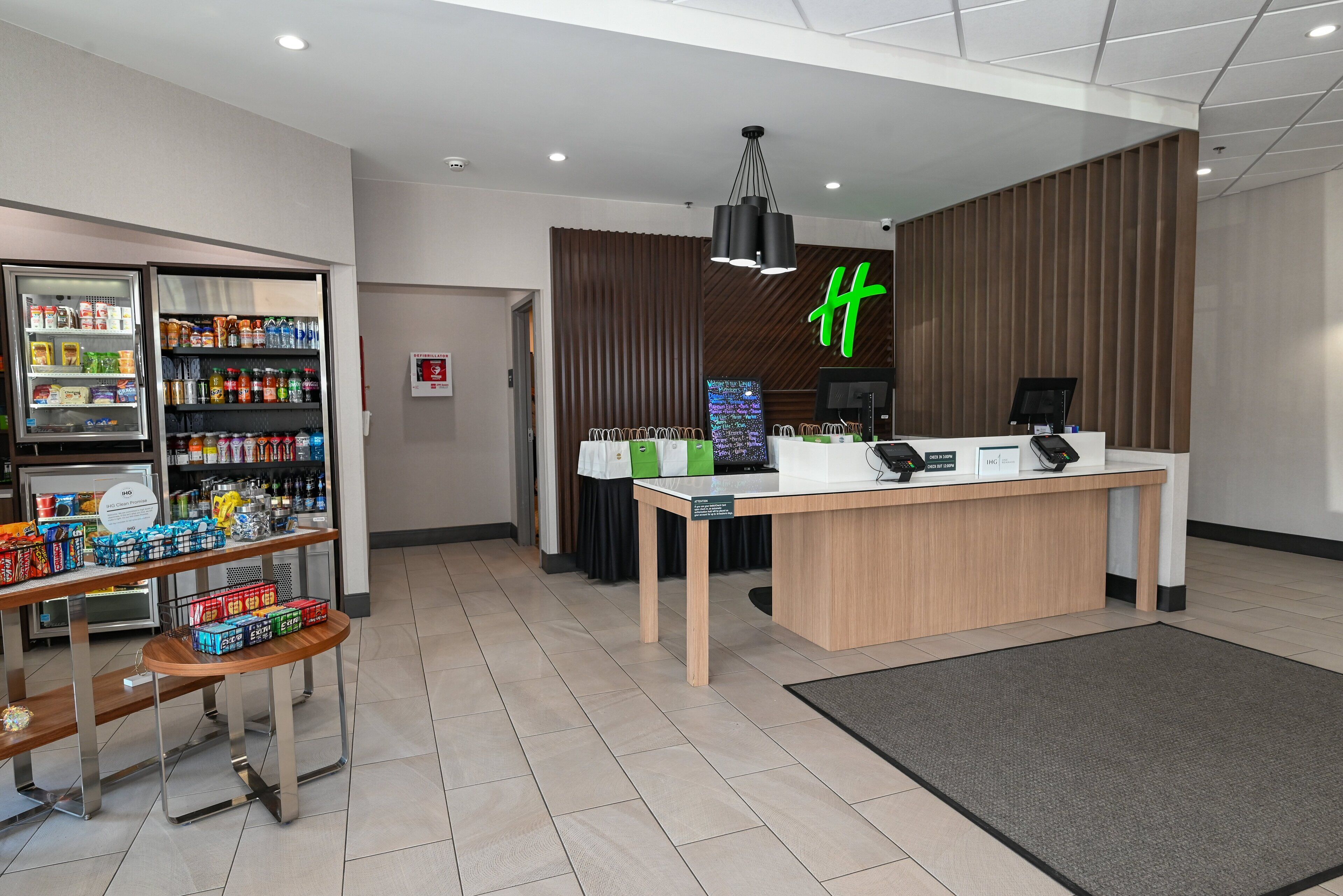 A reception area with a counter, a refrigerator stocked with beverages, and a sign with a green 'H'.