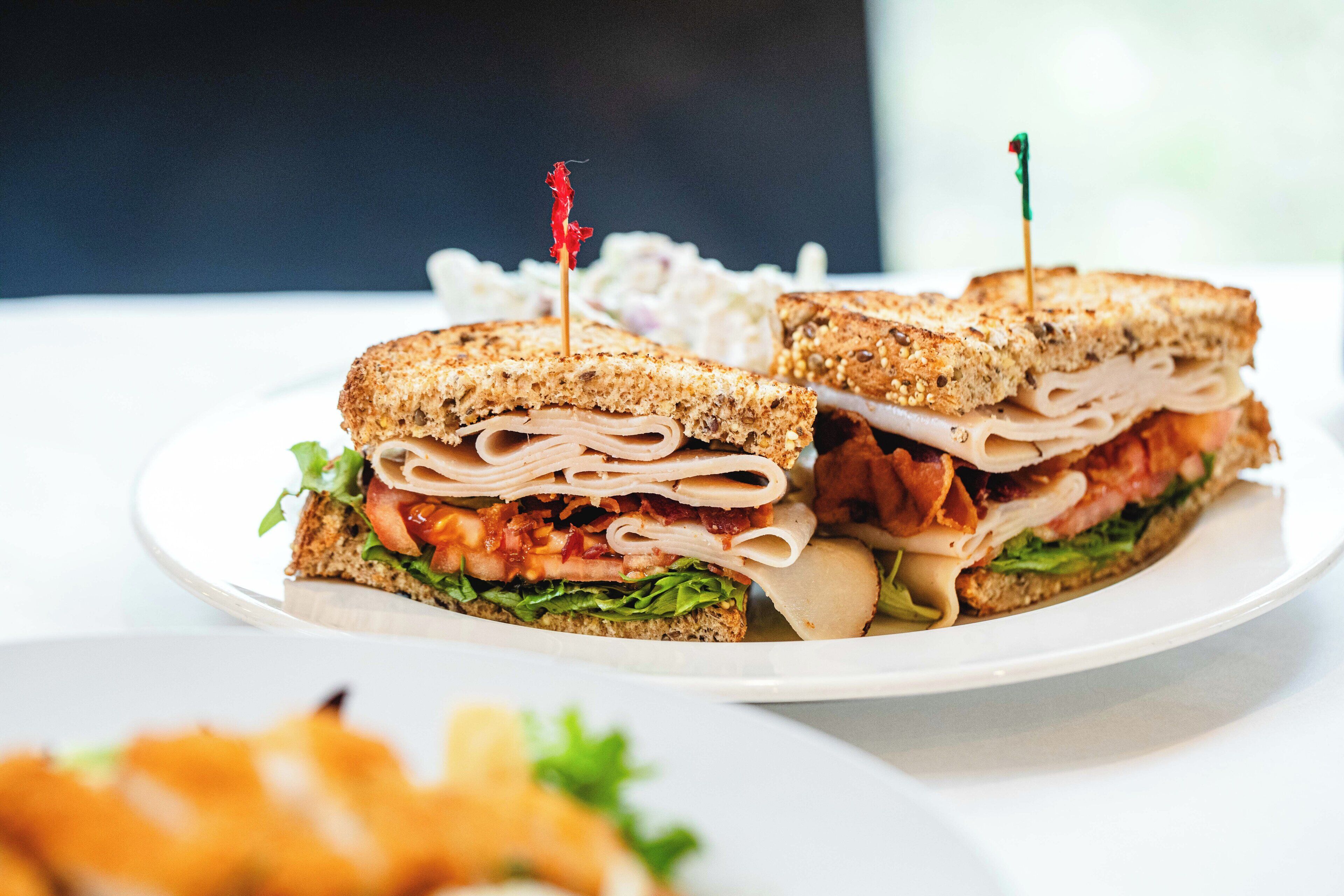 Un sándwich con capas visibles de carne, lechuga y tomate, sujeto con un palillo.