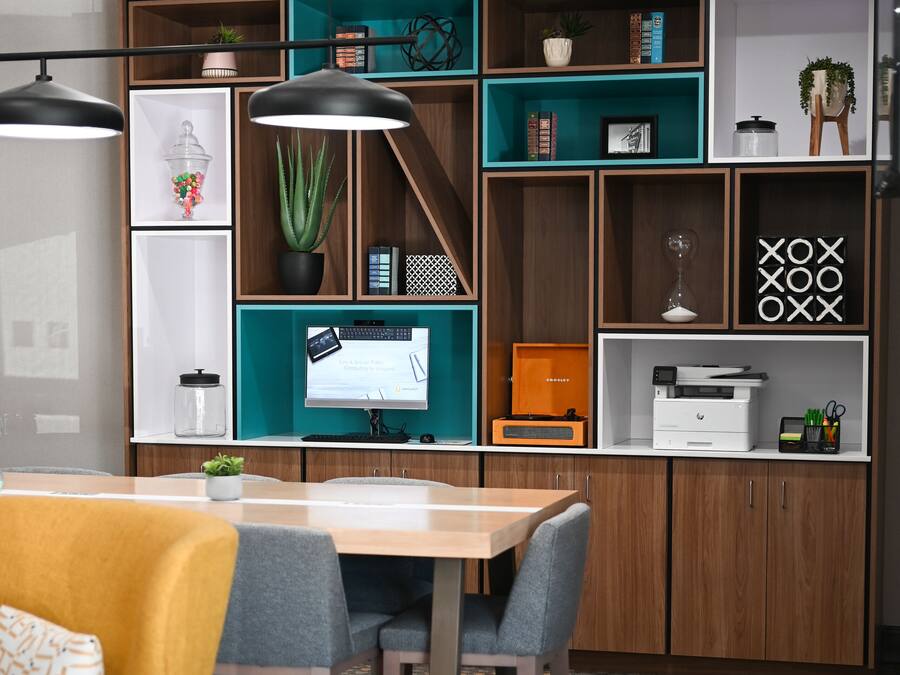 Un espacio de oficina moderno con un escritorio de madera, dos sillas, una computadora y estanterías con diversos objetos.