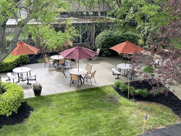 An outdoor patio area with round tables and chairs, surrounded by greenery and umbrellas. - Holiday Inn Cleveland-Mayfield by IHG (Mayfield)
