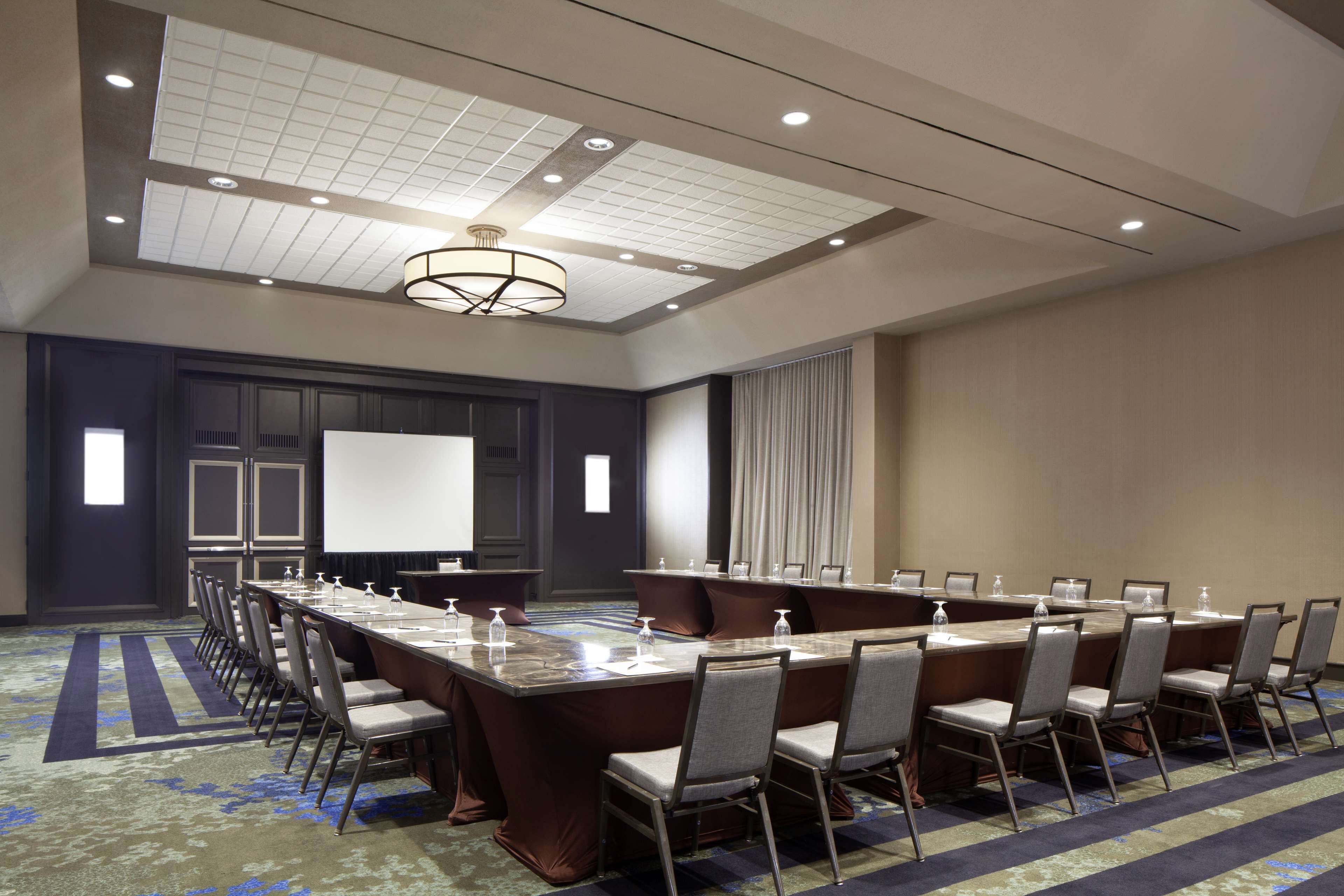A conference room with a long table, chairs, a projector screen, and a carpeted floor.