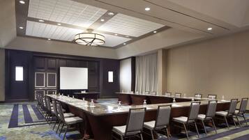 A conference room with a long table, chairs, a projector screen, and a carpeted floor.