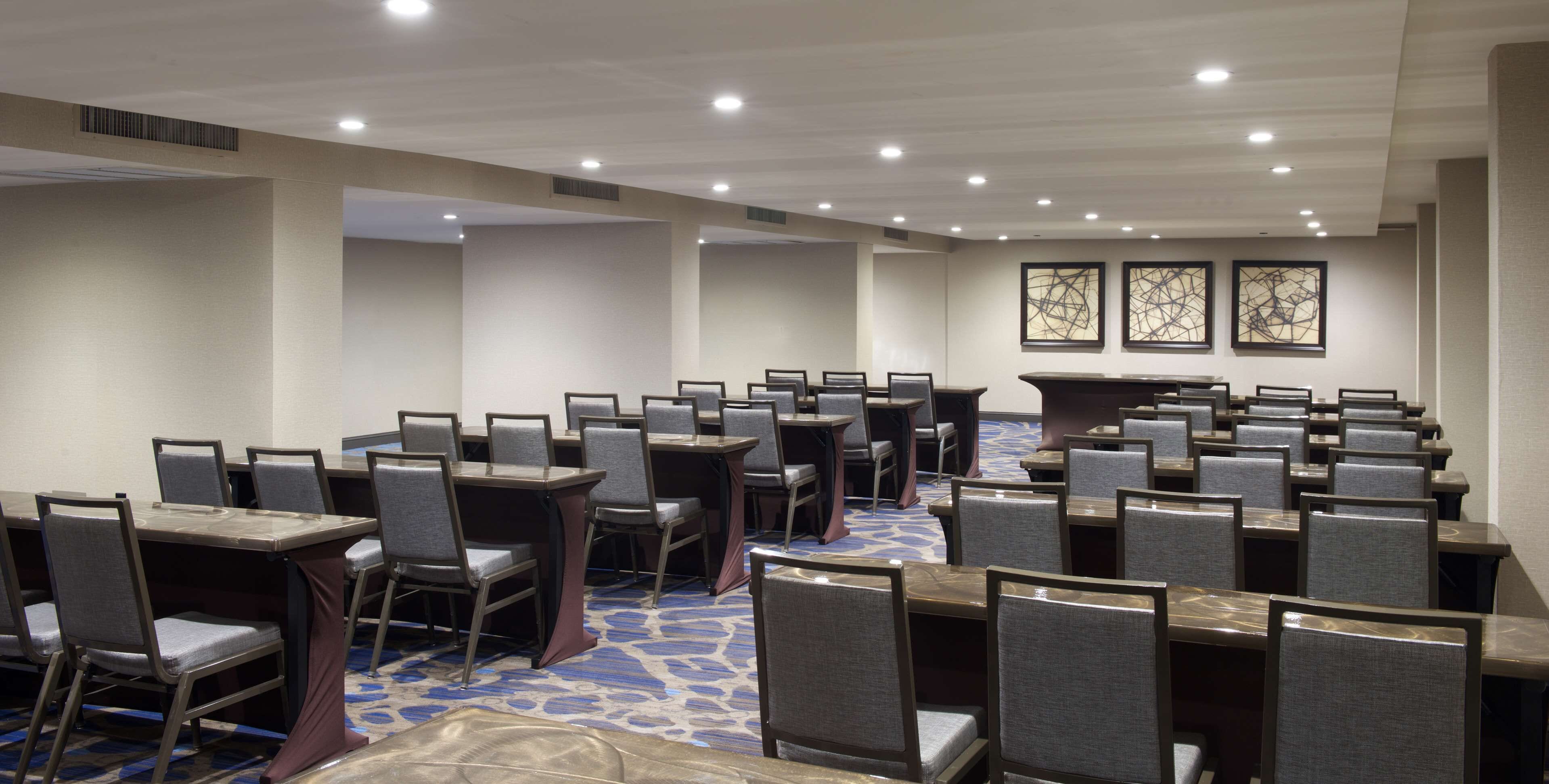 Un salón de conferencias con varias mesas y sillas, dispuestas en filas.