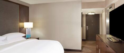 Una habitación de hotel con una cama, una mesita de noche con lámpara, un aparador y un televisor.