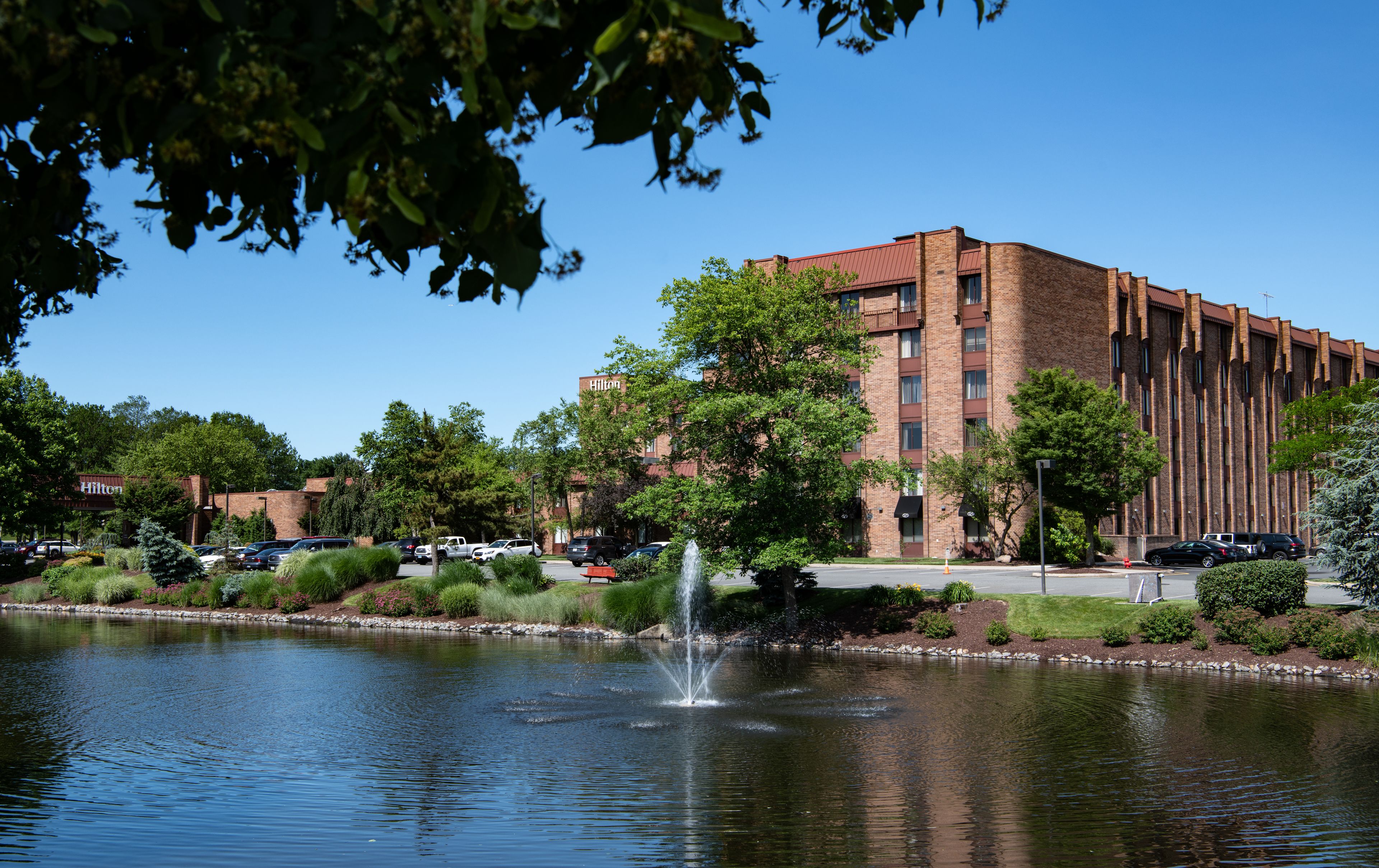 A hotel with a brick facade, a fountain, and a parking lot.