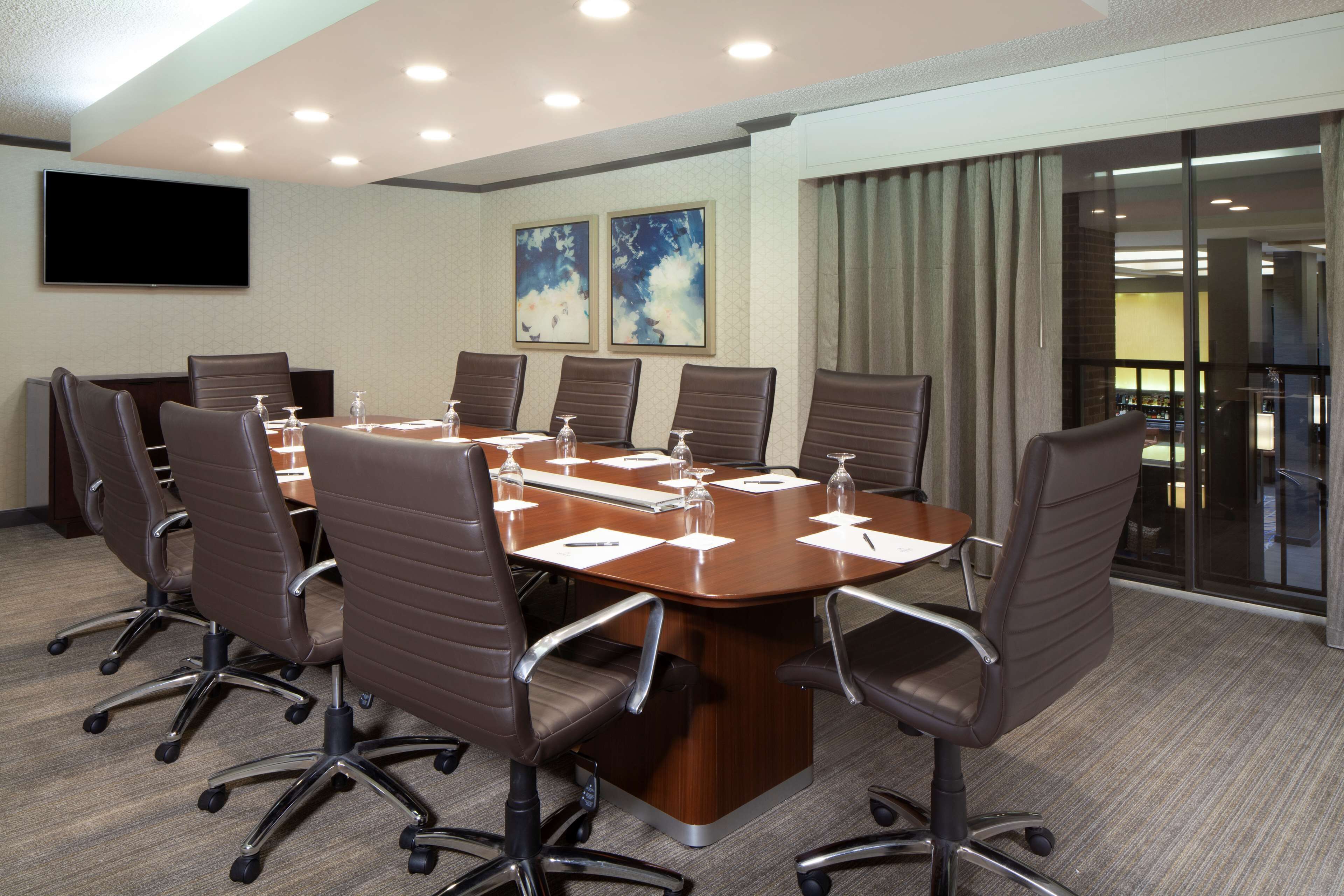 A conference room with a large table, six chairs, a flat-screen TV, and two framed artworks on the wall.