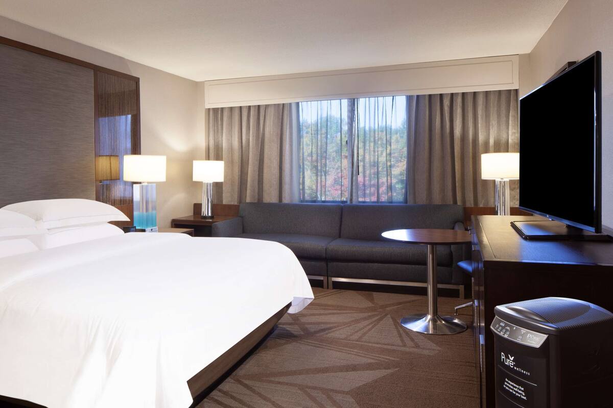 Quarto de hotel com uma cama grande, um sofá, uma TV e uma poltrona de massagem.