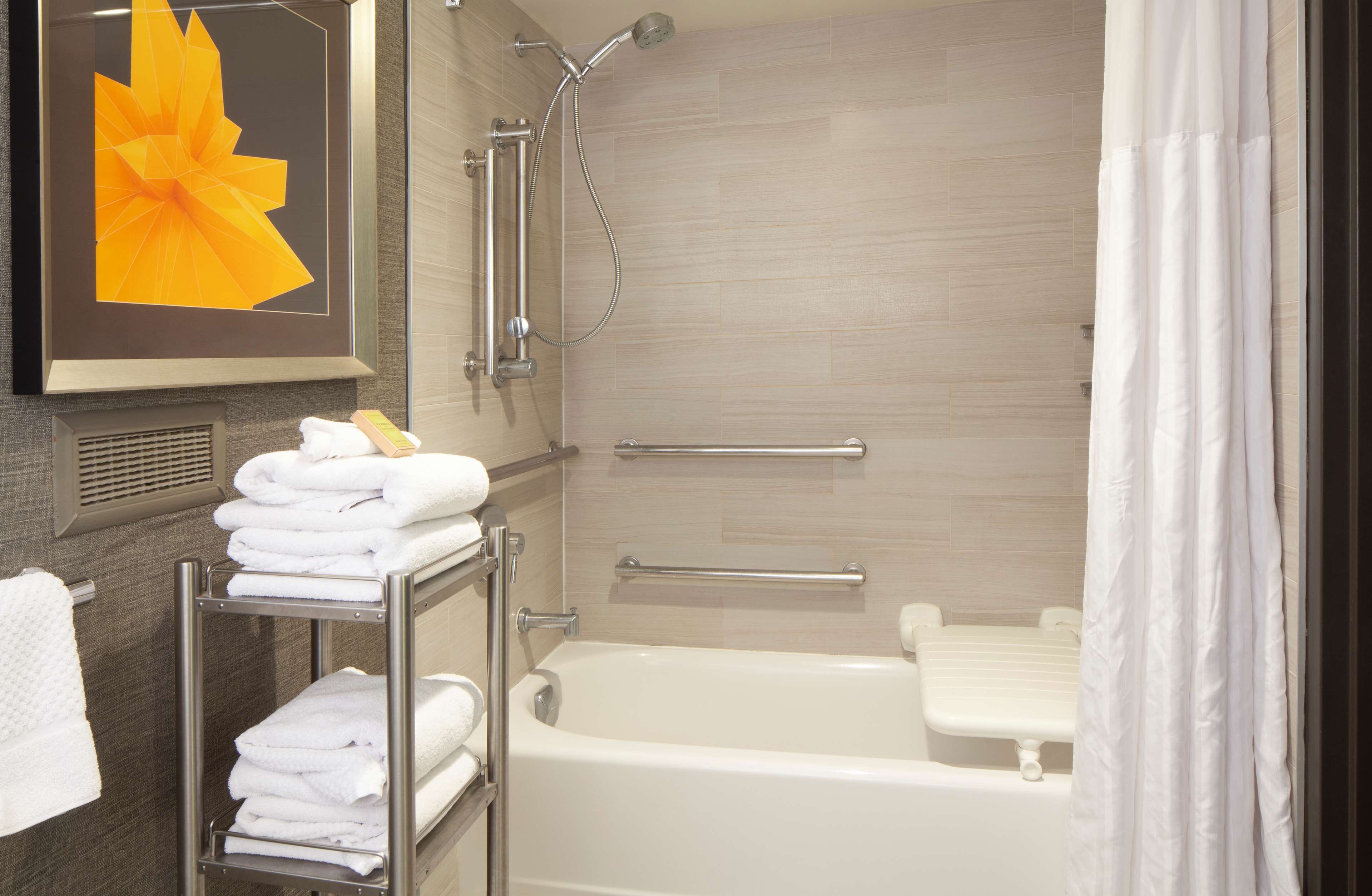 A modern bathroom with a bathtub, shower, and a towel rack with folded towels.