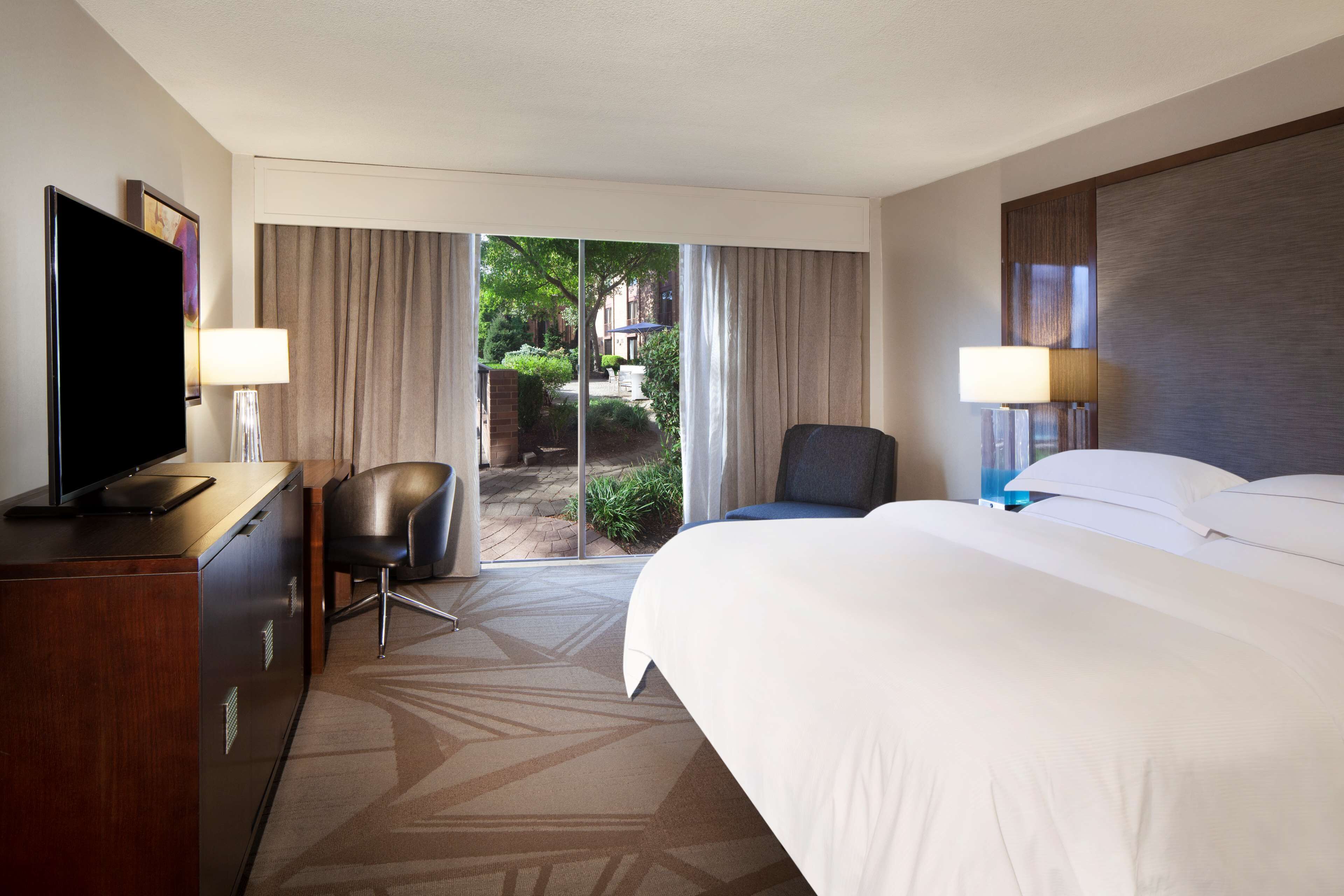Habitación de hotel con cama, escritorio con televisor, una silla y vista al exterior.