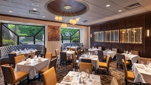 Un restaurant avec des tables rondes, des sièges confortables et une vue sur les arbres grâce à de grandes fenêtres.