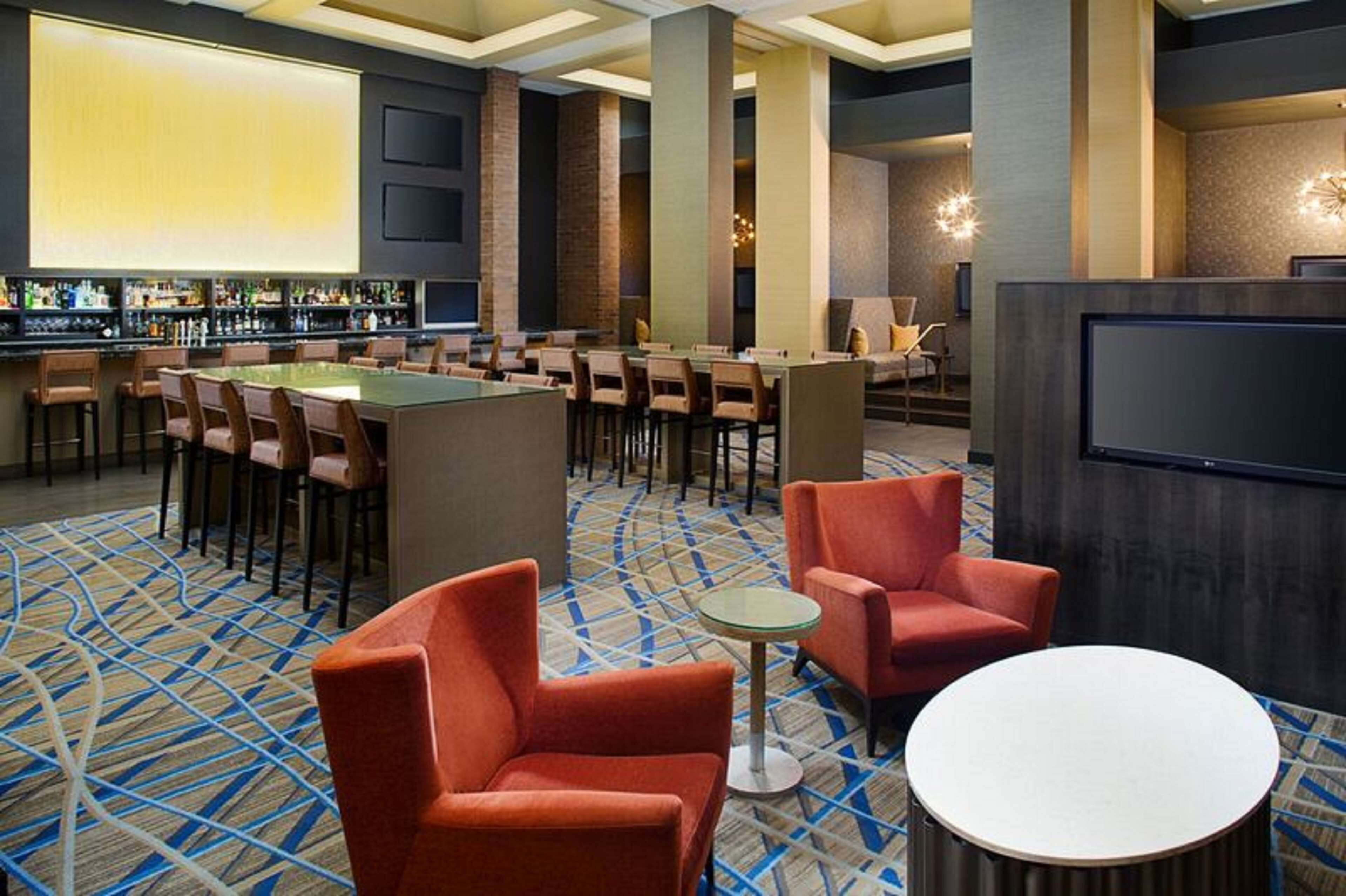 Un vestíbulo de hotel con una zona de bar, arreglos de asientos y una pantalla de televisión.