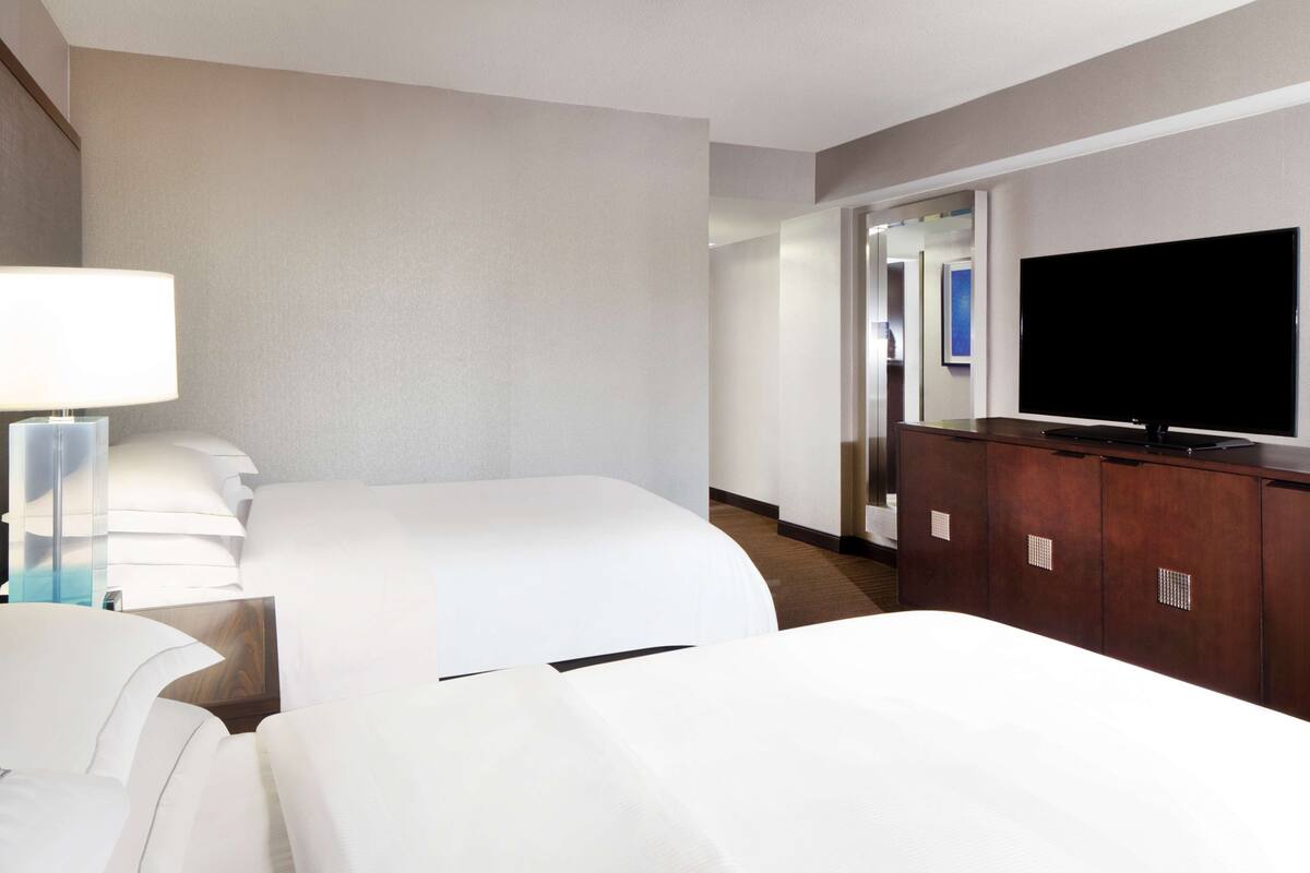 Quarto de hotel com duas camas, uma televisão e uma cômoda de madeira.