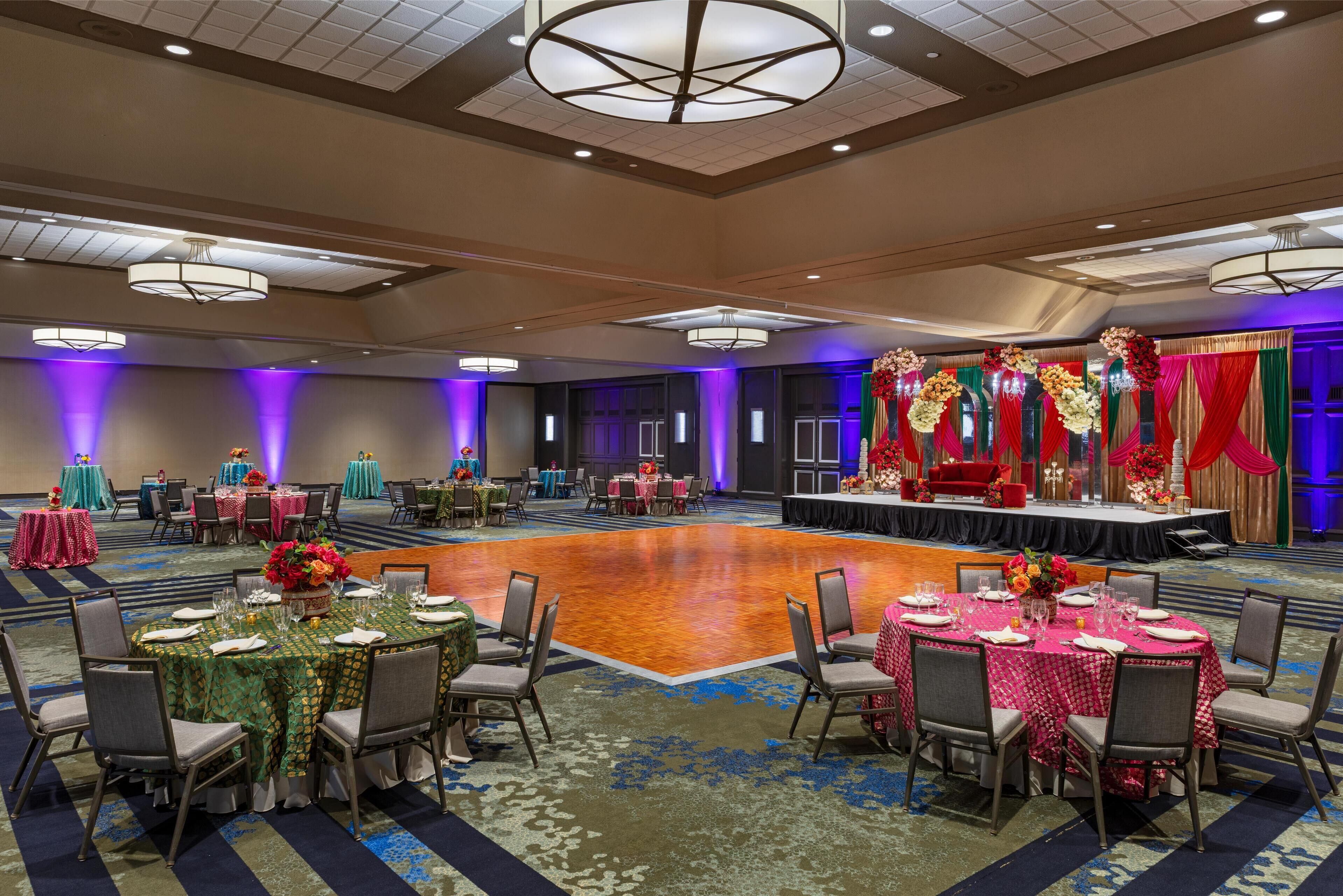 Une salle de banquet avec des tables rondes, des chaises et une scène décorée de fleurs.