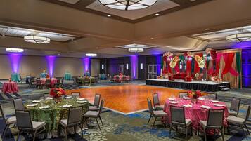 Une salle de banquet avec des tables rondes, des chaises et une scène décorée de fleurs.