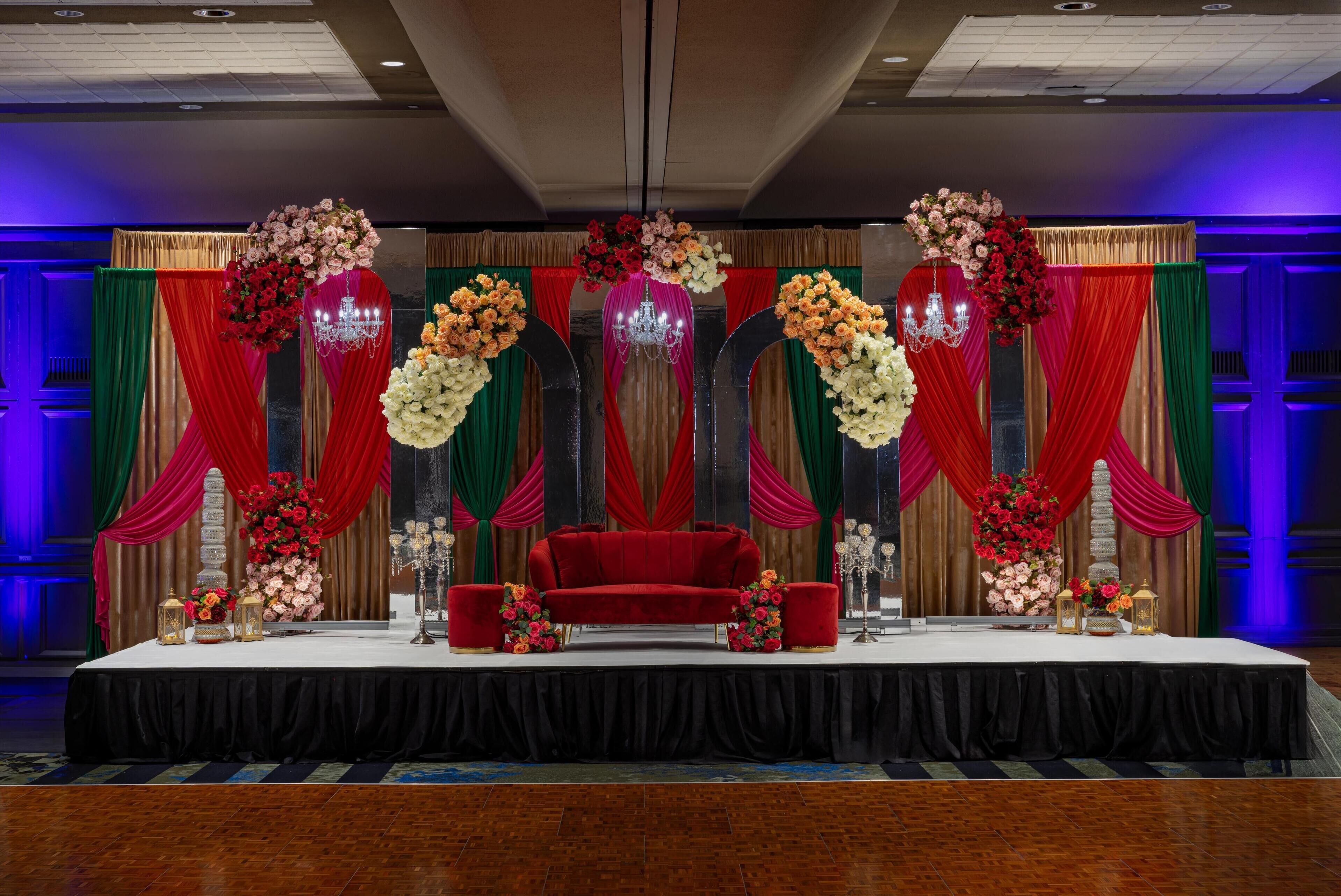 Un escenario con un sofá rojo, arreglos florales y cortinas drapeadas.