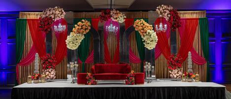 Un escenario con un sofá rojo, arreglos florales y cortinas drapeadas.