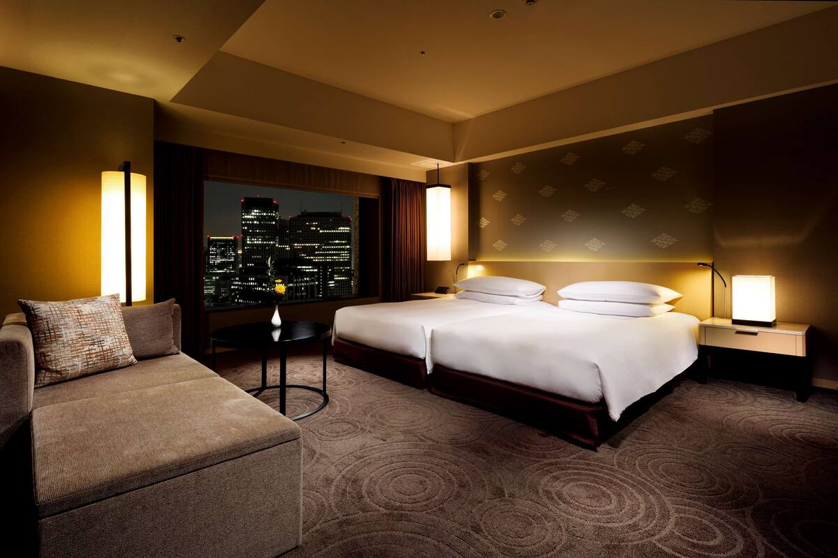 A hotel room with a large bed, a sofa, a desk, and a view of the city at night.