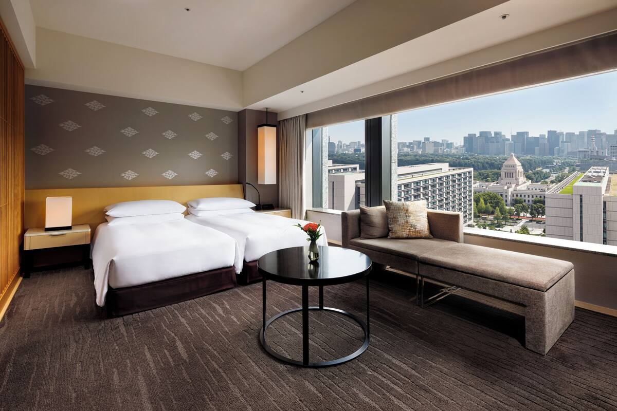 A hotel room with a large bed, a sofa, a round table, and a city view.