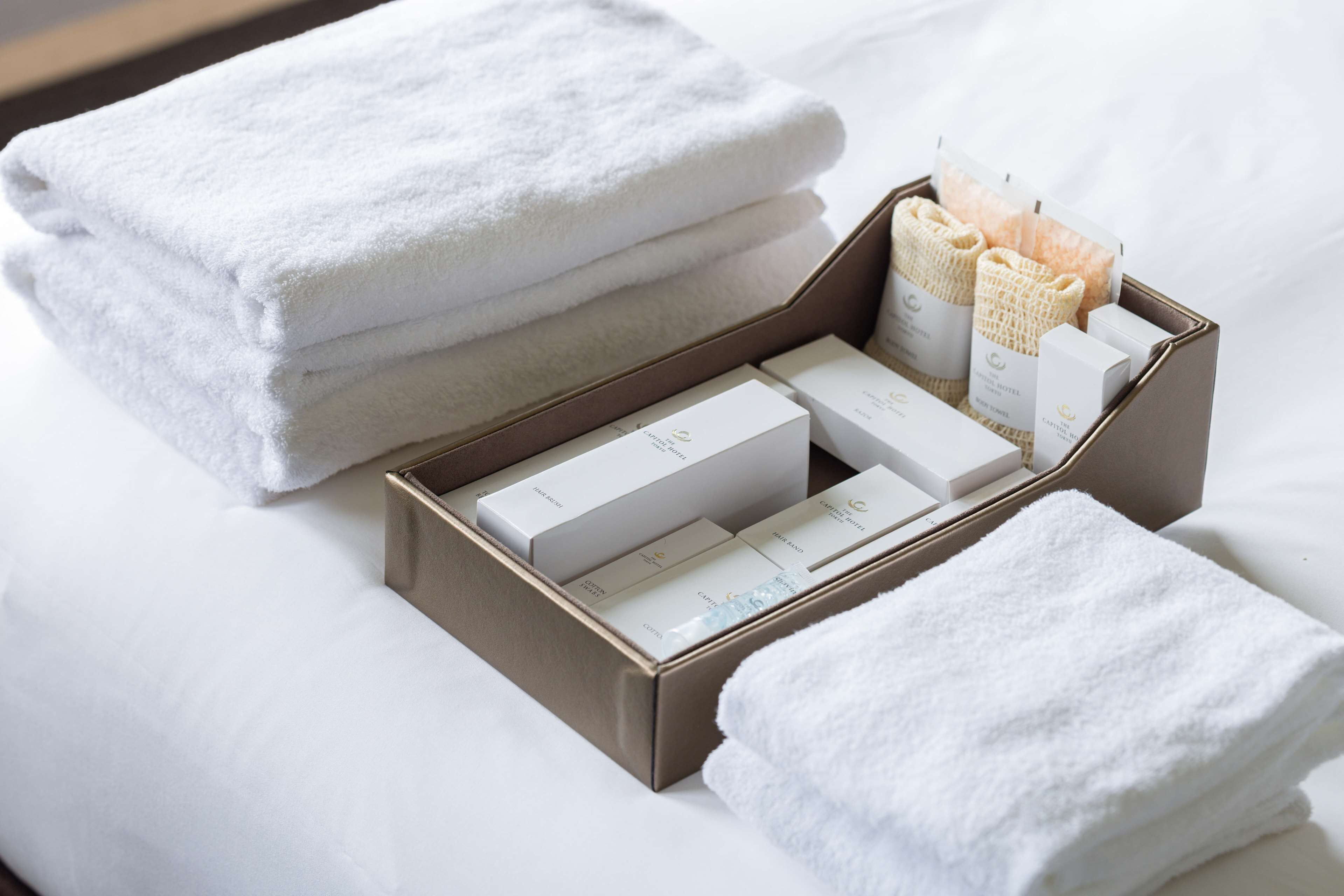 A neatly arranged set of white towels and toiletries in a wooden box on a bed.