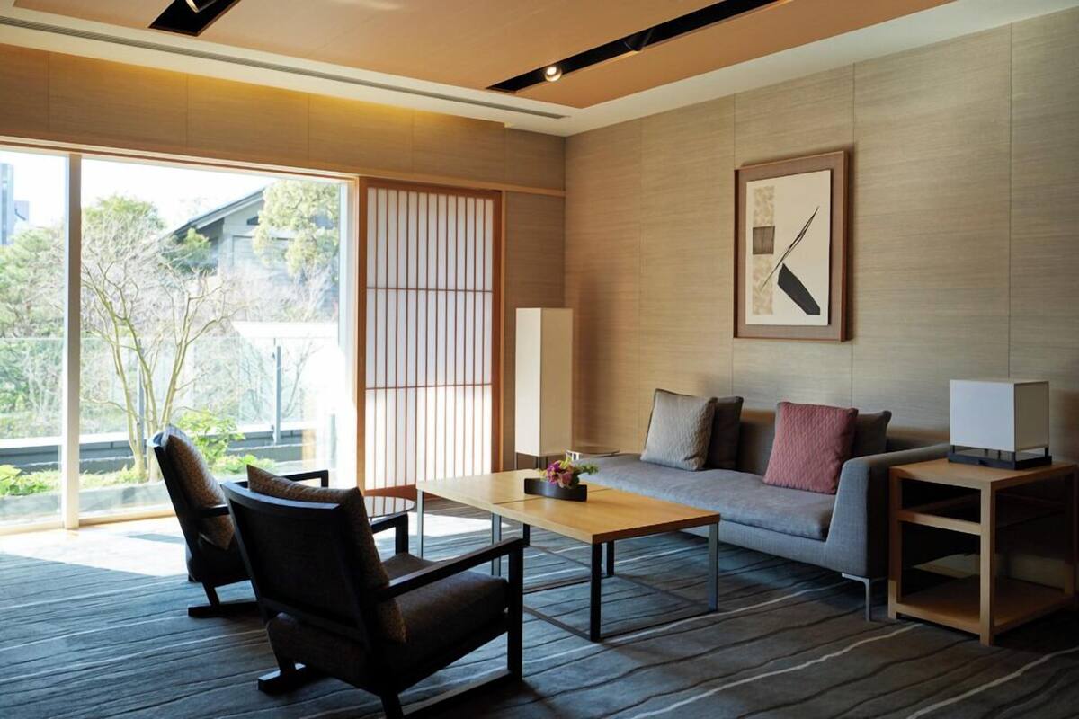A modern living room with a sofa, coffee table, and chairs, large windows, and a framed picture on the wall.