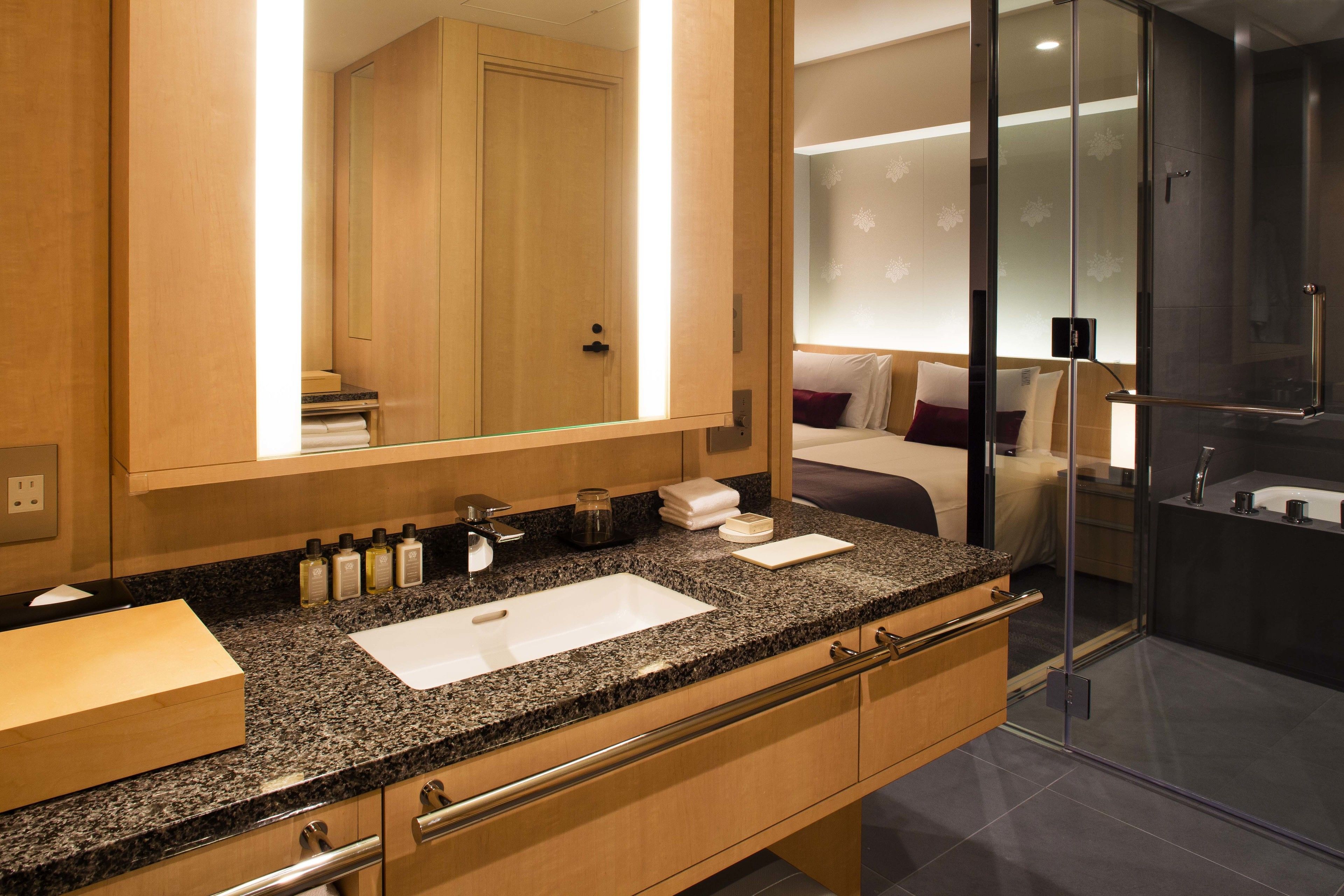 A modern bathroom with a granite countertop, a large mirror, and a glass shower enclosure.