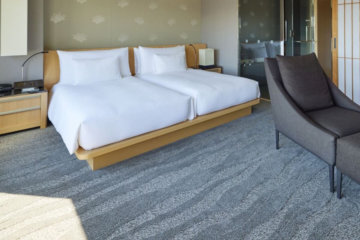 A hotel room with a large bed, a bedside table, a chair, a mirror, and a sliding door leading to a bathroom.