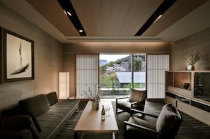 A modern living room with a sofa, armchair, and coffee table. There is a large window with a view of trees and a building.