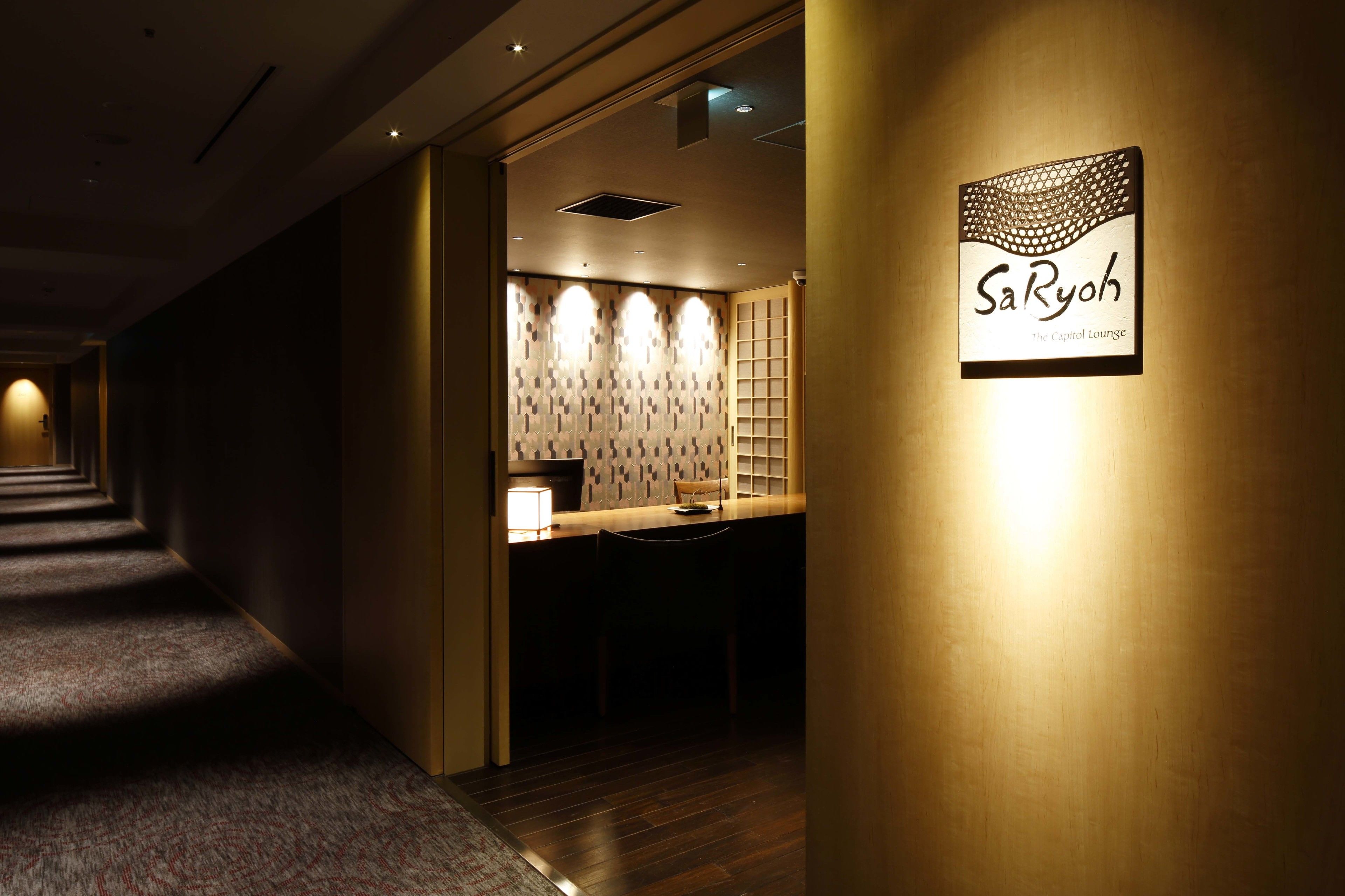 Corredor que leva a uma área de recepção com uma placa indicando "SaRyoh The Capitol Lounge".