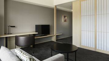 A modern hotel room with a sofa, a small round table, a desk with a television, and a sliding shoji screen.