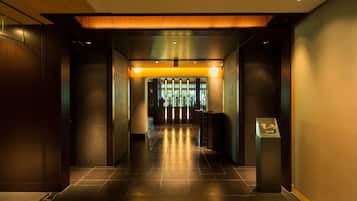 A modern hotel lobby with a dark wood floor, a reception desk, and a display case.