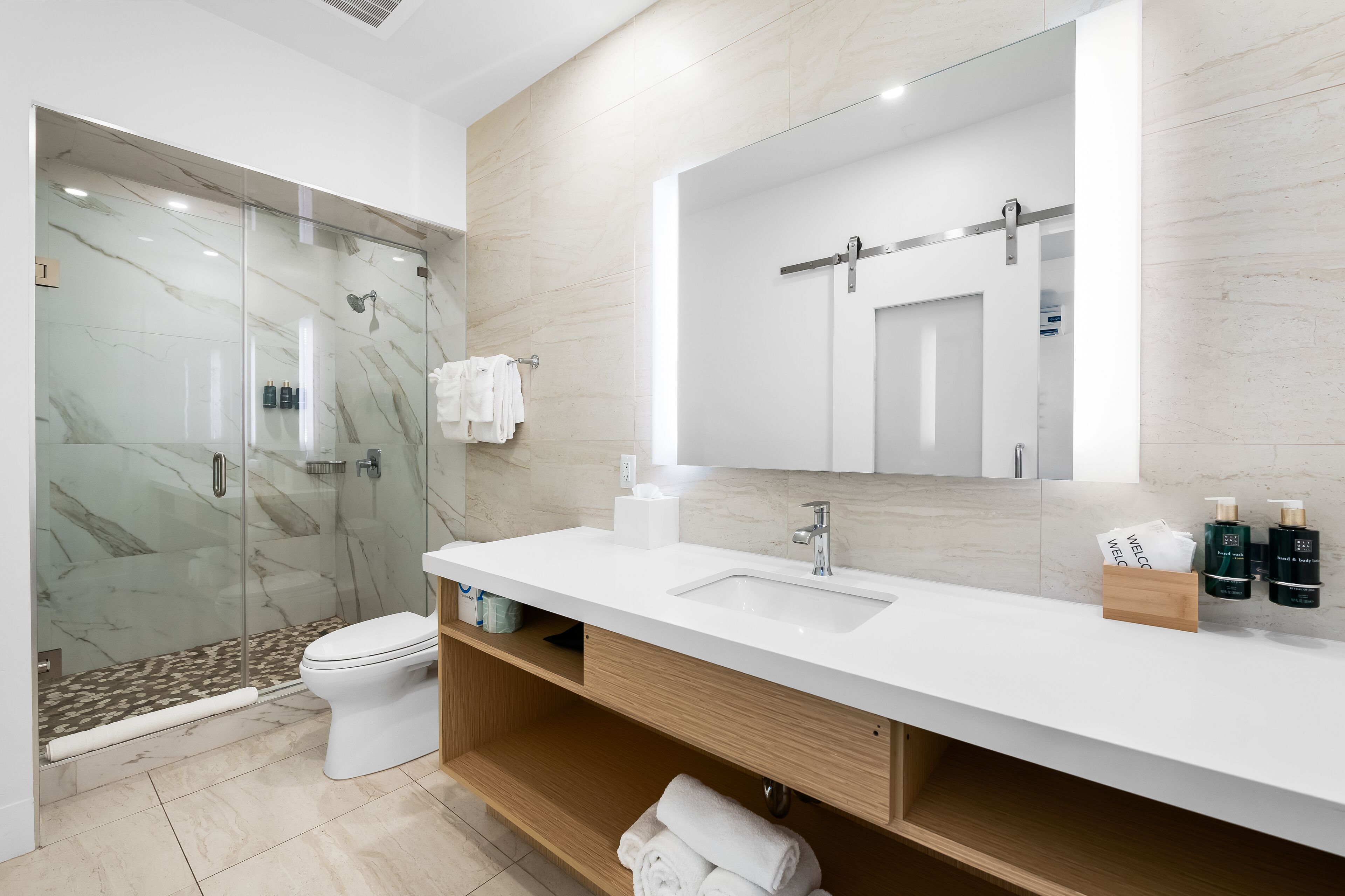 A modern bathroom with a glass-enclosed shower, a white sink, and a large mirror.