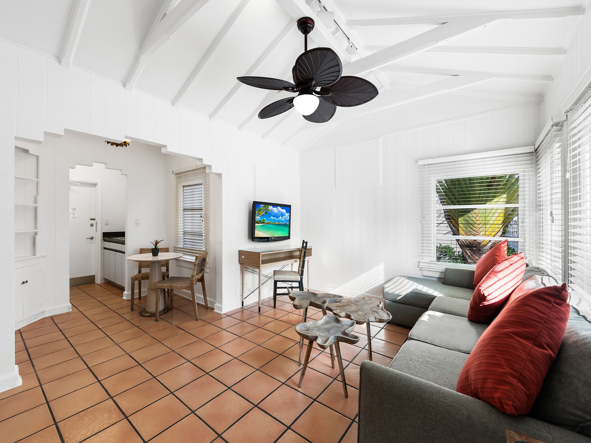 A spacious living area with a ceiling fan, a television, and a sofa with red cushions.