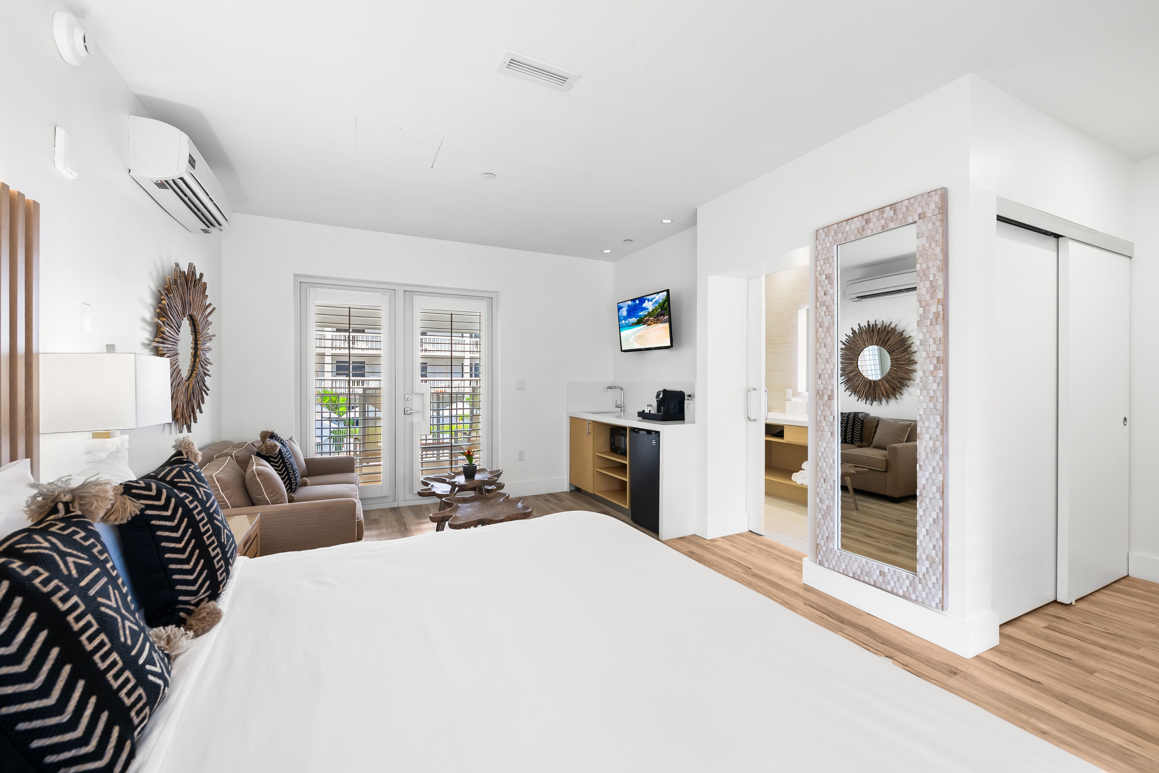 A modern hotel room with a large bed, a sofa, a dining table, and a kitchen area.