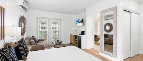 A modern hotel room with a large bed, a sofa, a dining table, and a kitchen area.