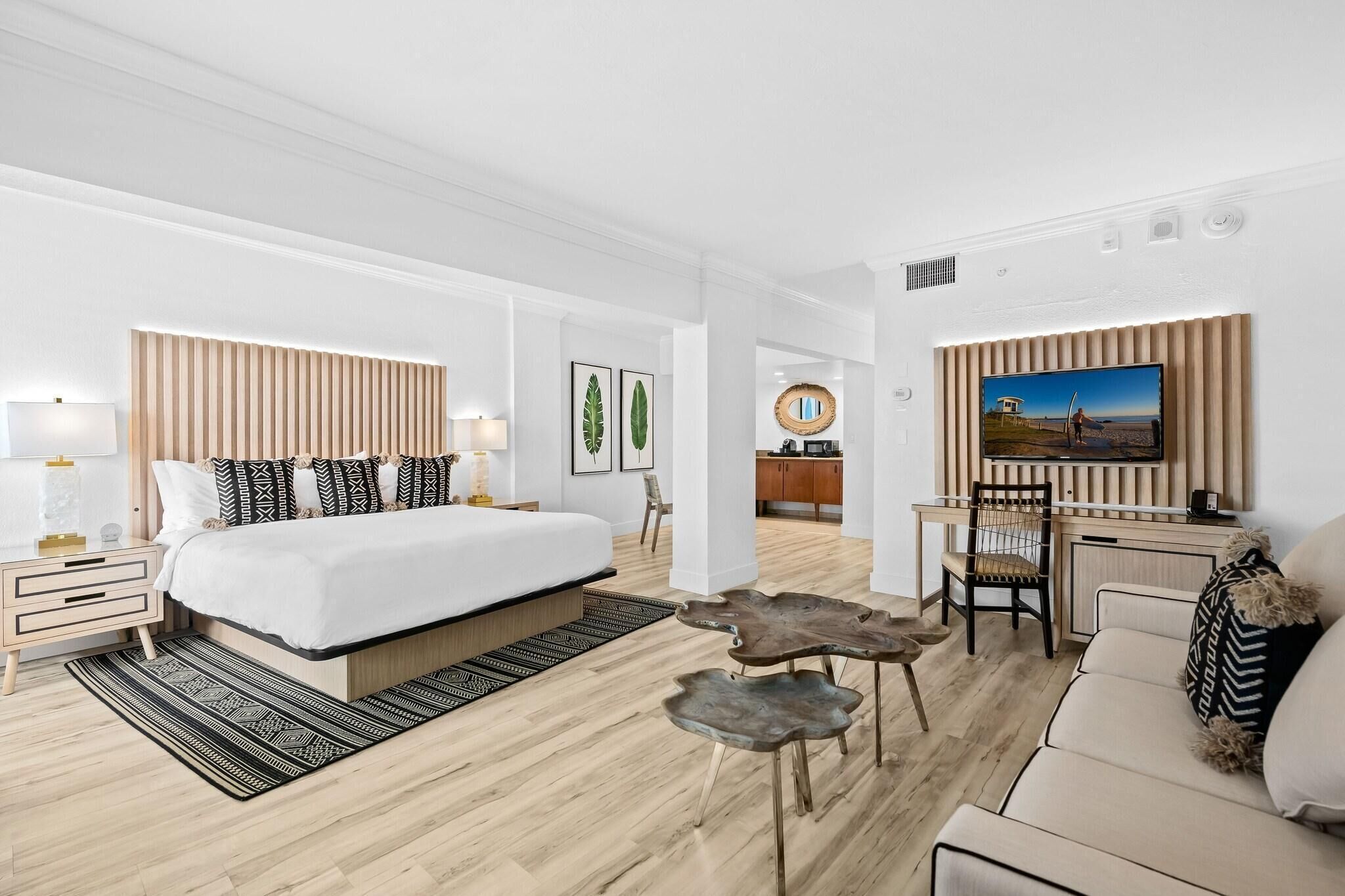 Una habitación de hotel moderna con una cama grande, un escritorio, un televisor y un sofá.
