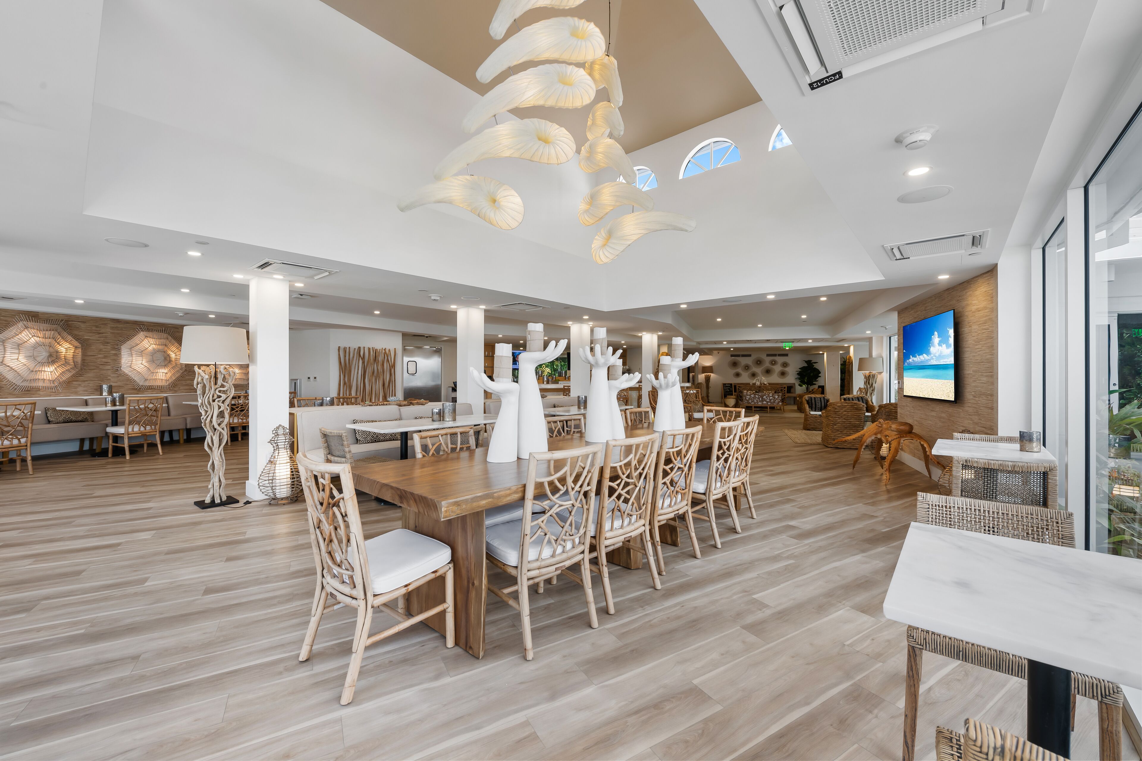 Un vaste espace dédié à la salle à manger, avec des tables et des chaises en bois, un design moderne au niveau du plafond et un grand écran de télévision.
