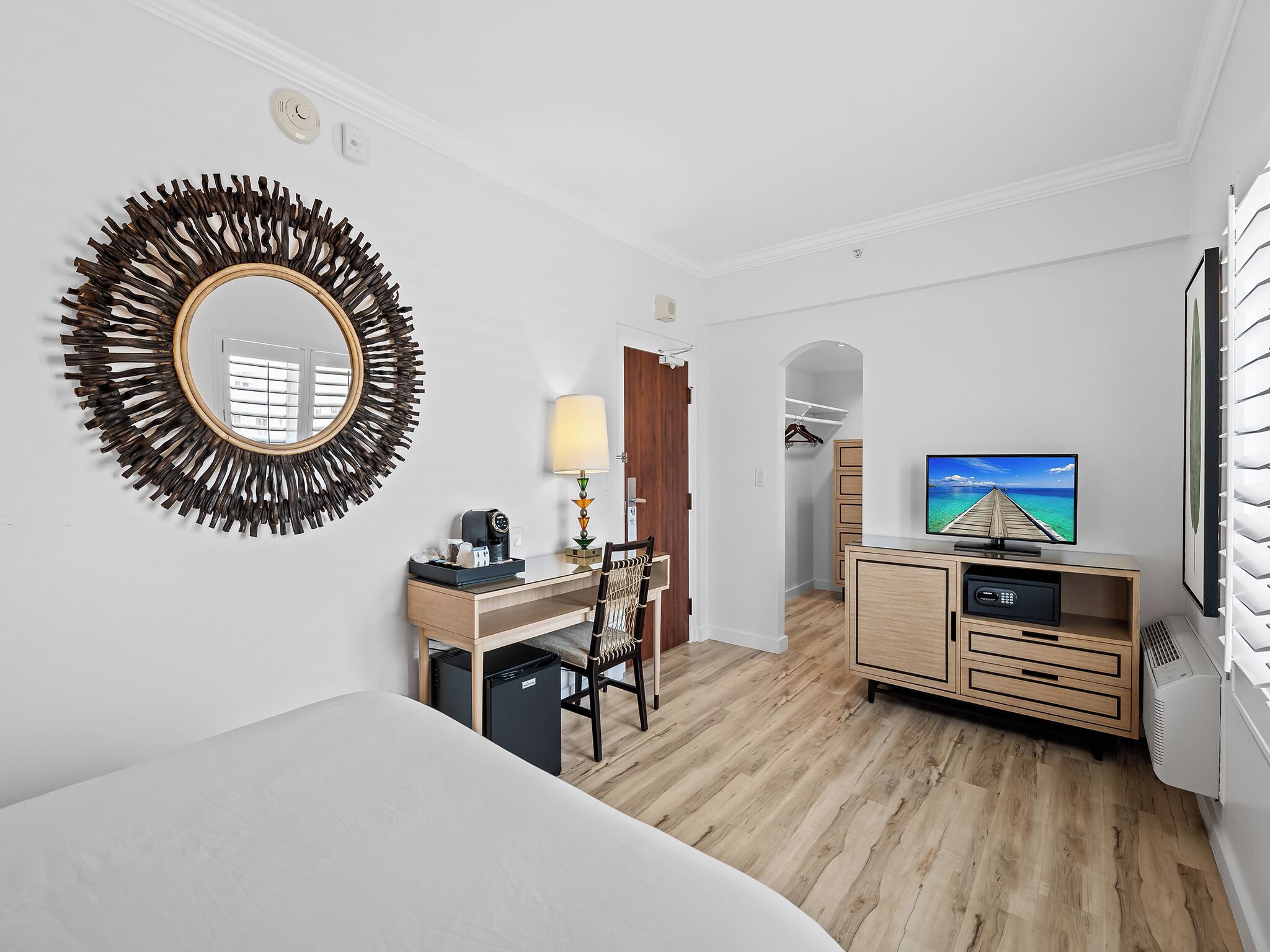 Habitación de hotel con cama, escritorio, silla, televisión y vestidor.