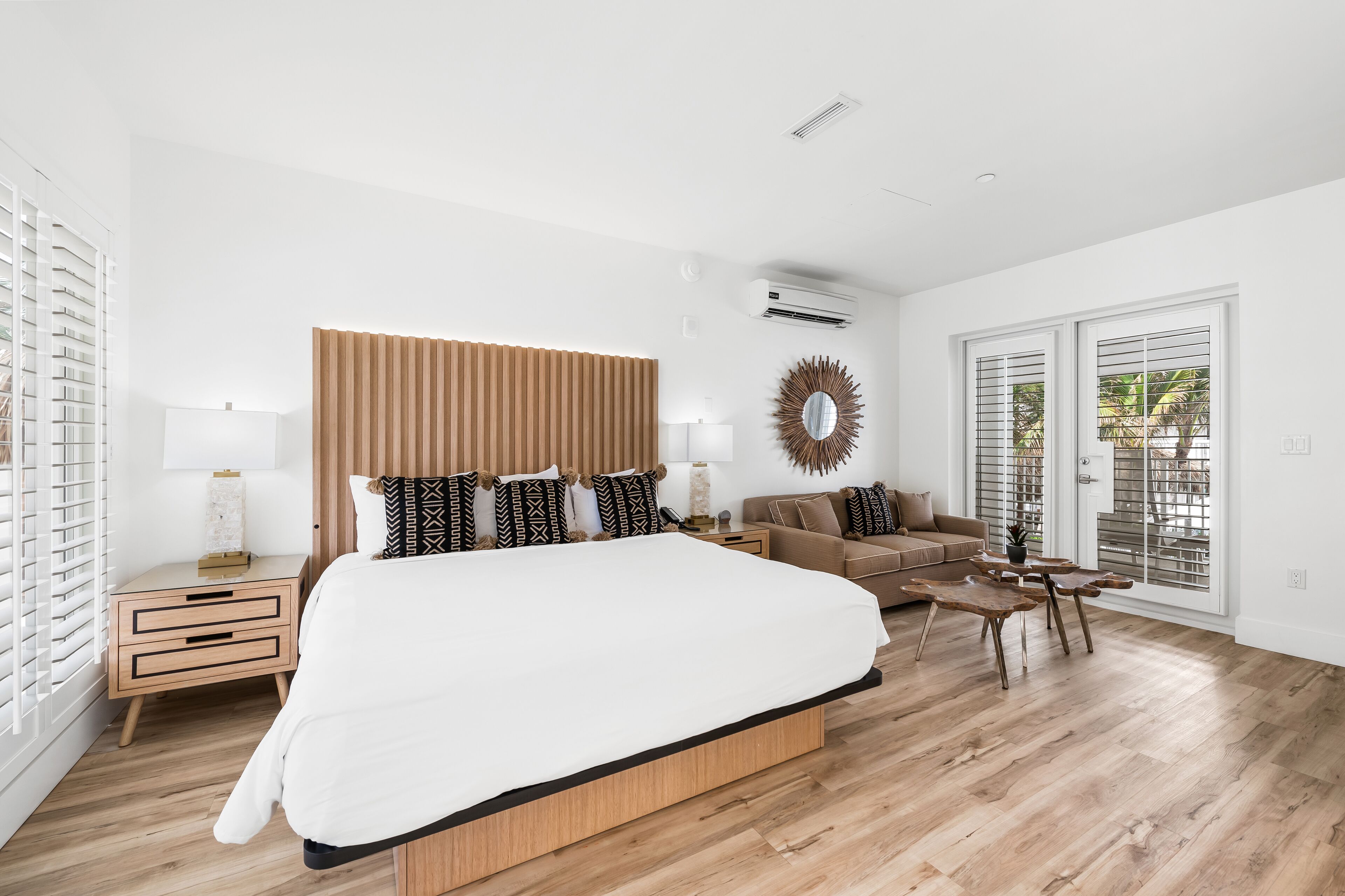 Une chambre moderne avec un grand lit, une tête de lit en bois, une table de chevet avec une lampe, un canapé et une table à manger.