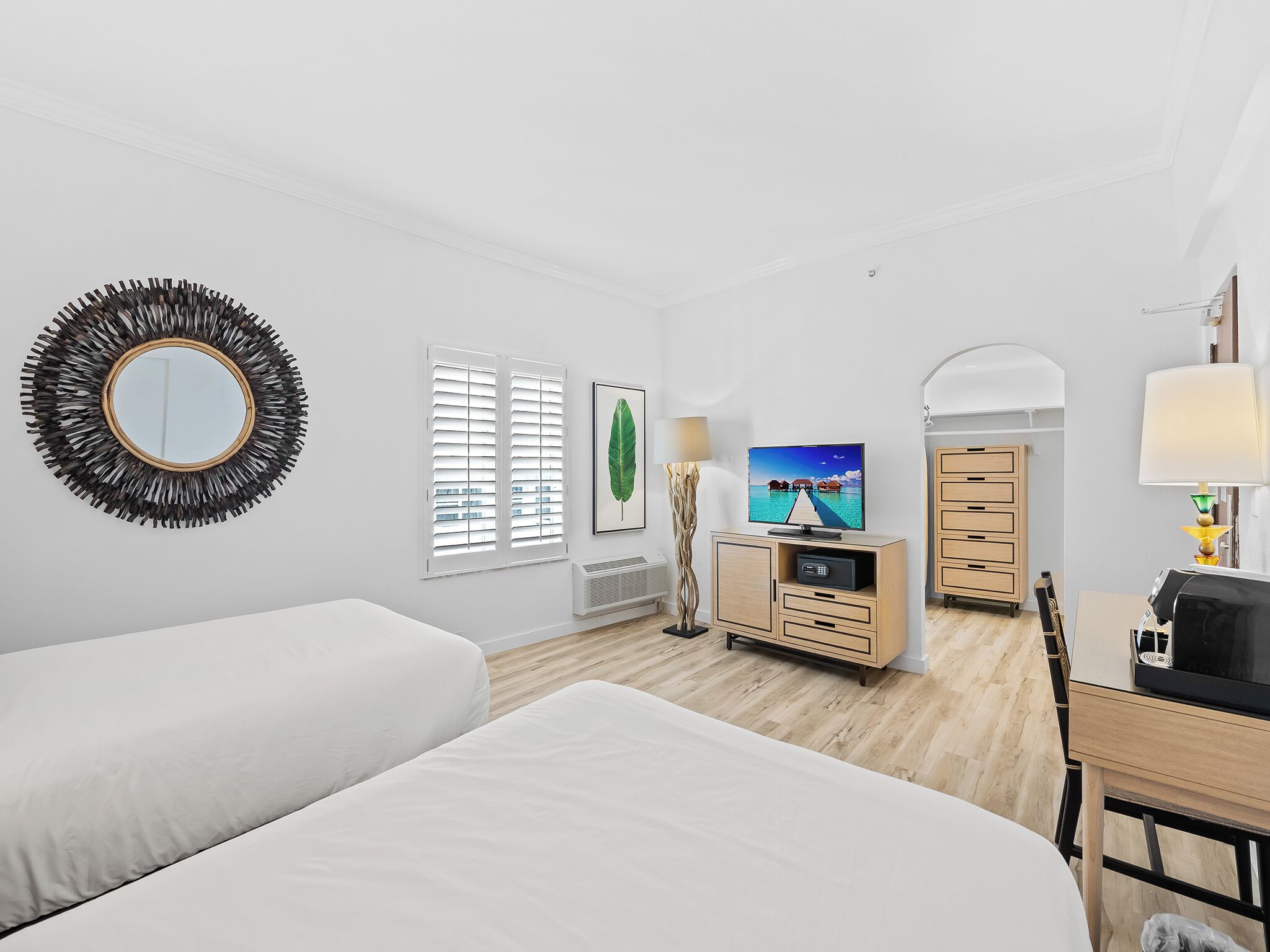 Habitación de hotel con dos camas, televisor, escritorio, lámpara y espejo.