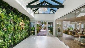 A modern hotel lobby with a green wall, glass doors leading to a pool area, and a clear view of the pool through the glass. - Beachcomber Resort & Club (Pompano Beach)