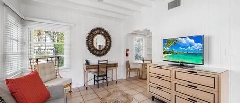 A spacious living room with a large TV, a wooden coffee table, a sofa, and a dining area with a chair and a table.