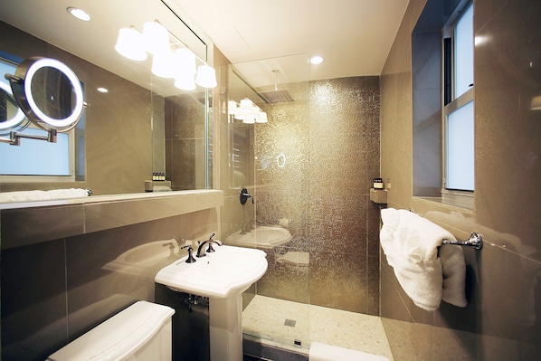 A modern bathroom with a glass shower enclosure, a white sink, and a large mirror with lights. - Cavalier Hotel South Beach (Miami Beach)