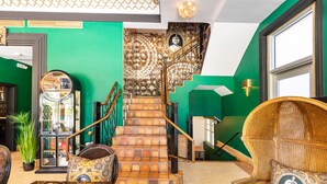 A staircase with a patterned wall, a rattan chair, and a mirror.