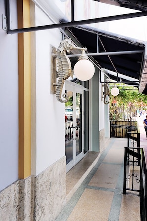 A covered walkway with a metal railing, a bench, and a door to a building.