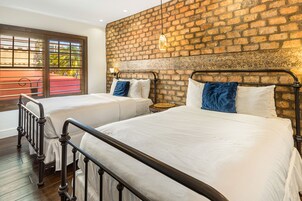 A room with two beds, a brick wall, and a window with a view of greenery.