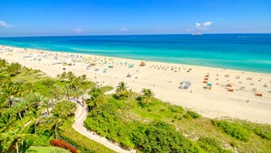 A beach with numerous umbrellas and sun loungers, a clear blue sky, and a distant cruise ship.